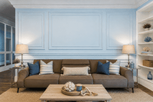 Coastal interior living room with crown molding, wall panel trim, blue walls, and neutral furniture